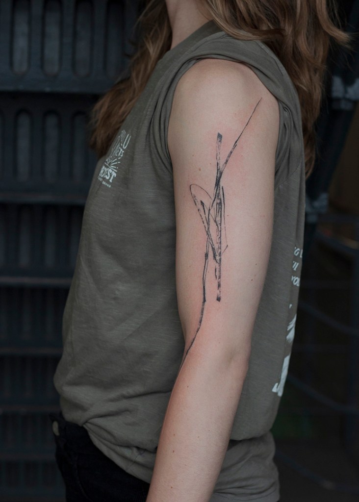 abstracte tattoo op linkerbovenarm. Lijnen met textuur, alsof het met inkt op de arm getekend is