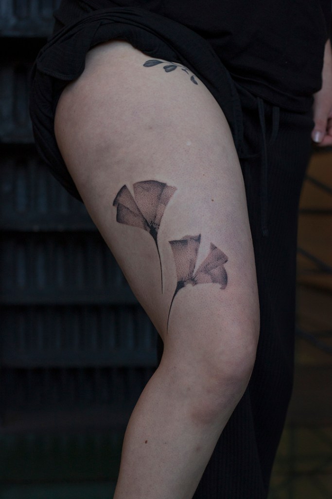 handpoke tattoo van twee ginkgo bladeren op de buitenkant het rechter bovenbeen, vlak boven de knie. Ongeveer 25 centimeter groot. De bladeren zien er breekbaar uit met veel gradaties