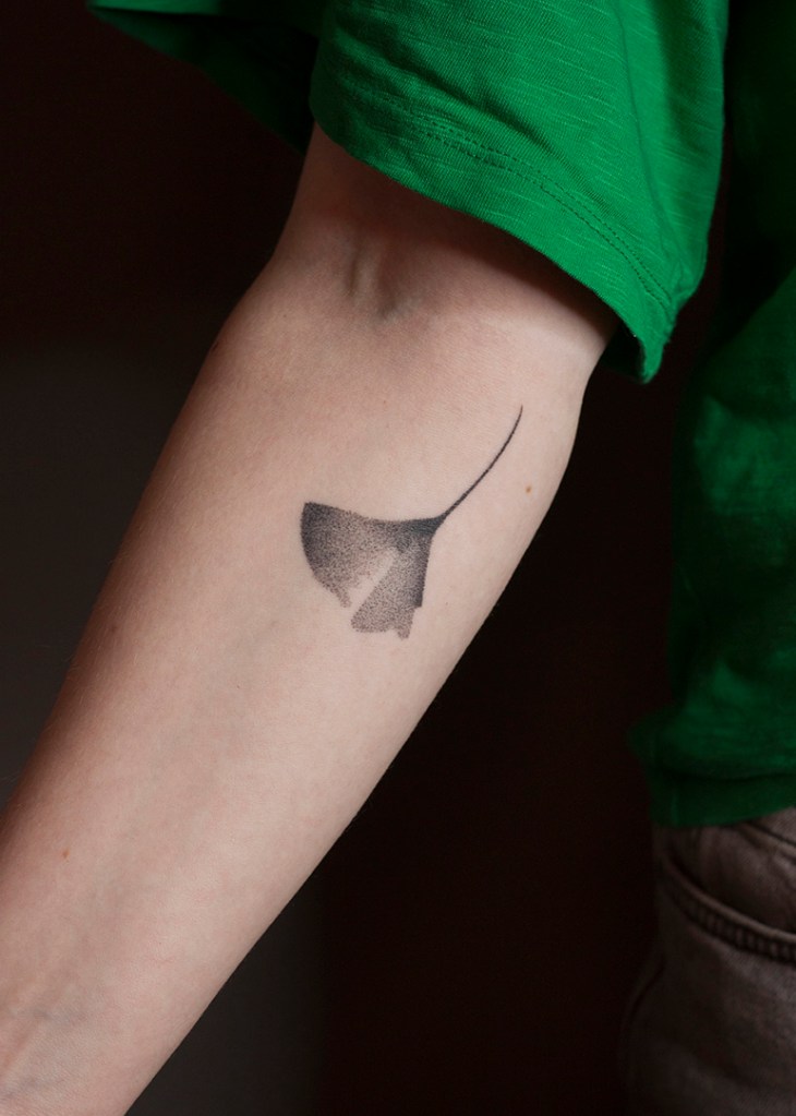 andpoke tattoo van een ginkgo blad op de onderkant van de rechter onderarm. Het blad ziet er breekbaar uit met veel gradaties