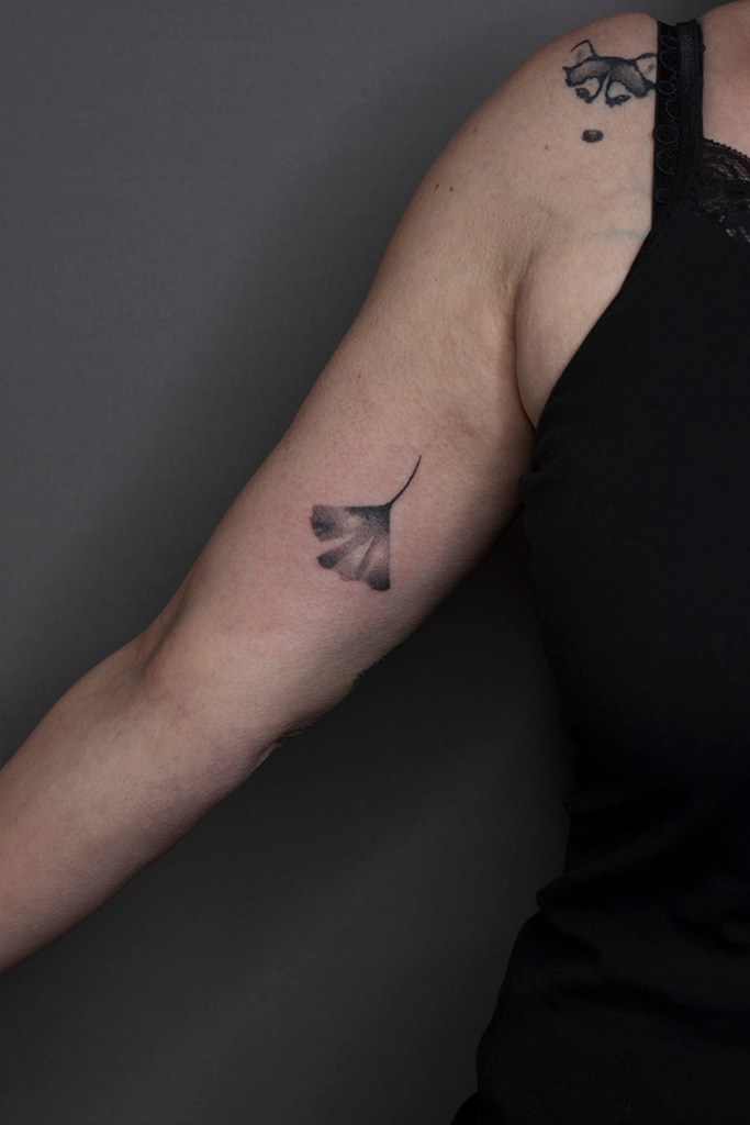 handpoke tattoo van een ginkgo blad op de rechter bicep. Het blad ziet er breekbaar uit met veel gradaties