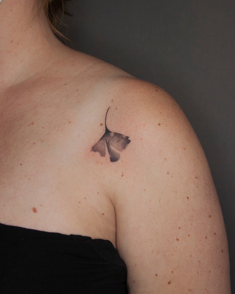 handpoke tattoo van een ginkgo blad op de voorkant van de linker schouder. Het blad ziet er breekbaar uit met veel gradaties