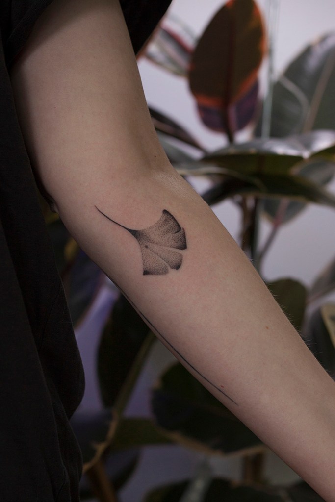 handpoke tattoo van een ginkgo blad op de achterkant van de linker onderarm, net onder de elleboogsplooi. Het blad ziet er breekbaar uit met veel gradaties
