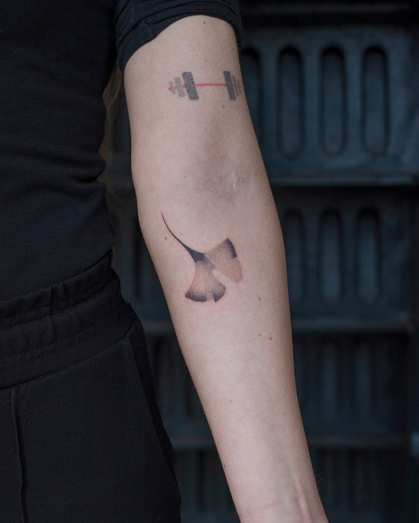 handpoke tattoo van een ginkgo blad op de achterkant van de linker onderarm, net onder de elleboogsplooi. Het blad ziet er breekbaar uit met veel gradaties