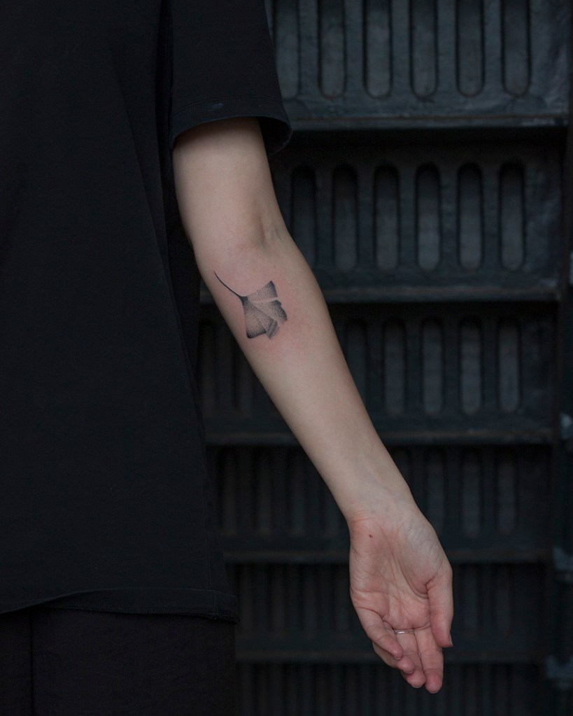handpoke tattoo van een ginkgo blad op de achterkant van de linker onderarm, net onder de elleboogsplooi. Het blad ziet er breekbaar uit met veel gradaties