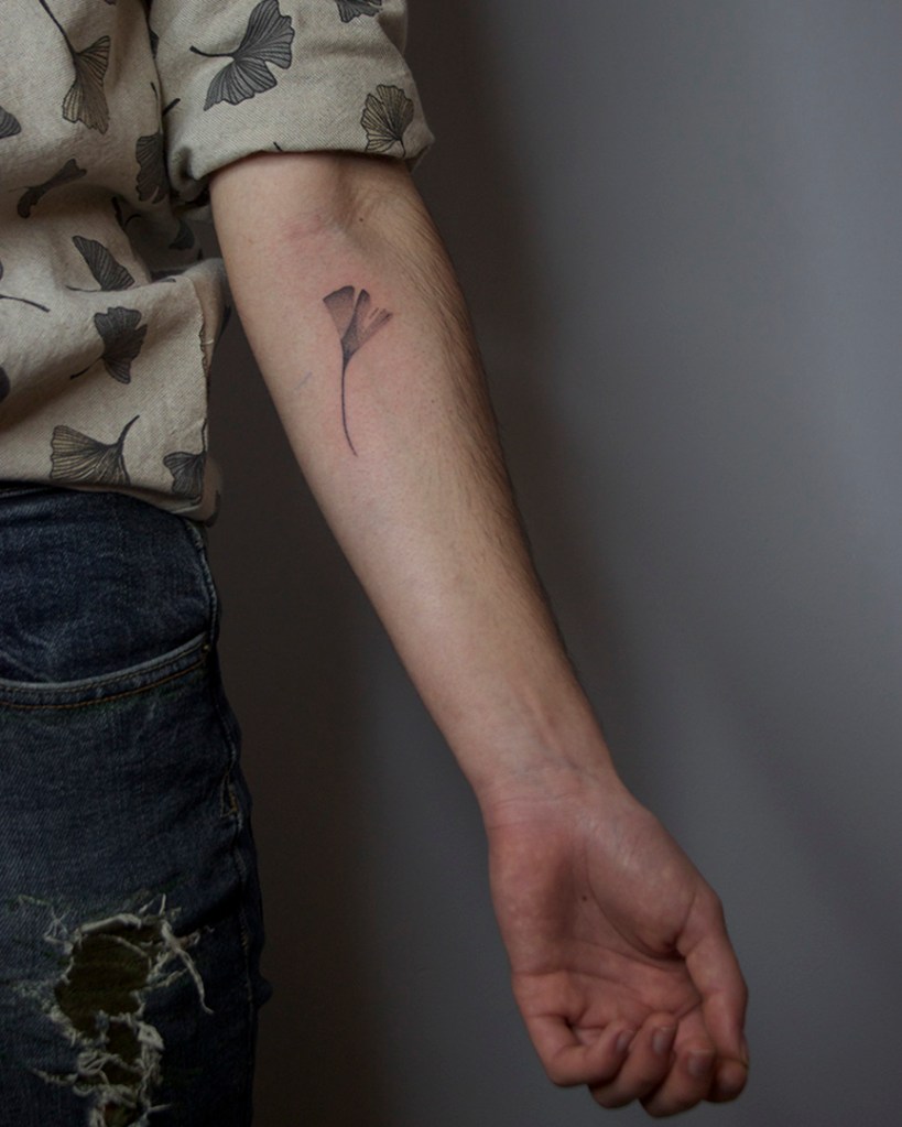 handpoke tattoo van een ginkgo blad op de achterkant van de linker onderarm, net onder de elleboogsplooi. Het blad ziet er breekbaar uit met veel gradaties