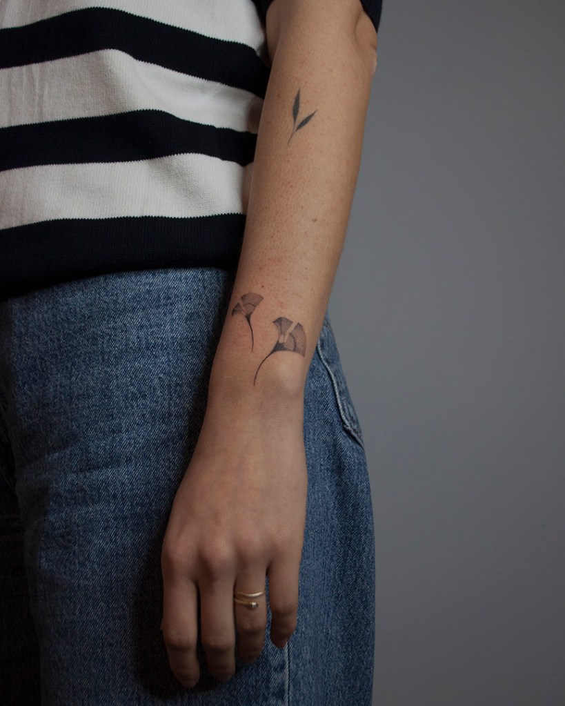 handpoke tattoo van twee ginkgo bladeren op de buitenkant de linker pols. De bladeren zien er breekbaar uit met veel gradaties