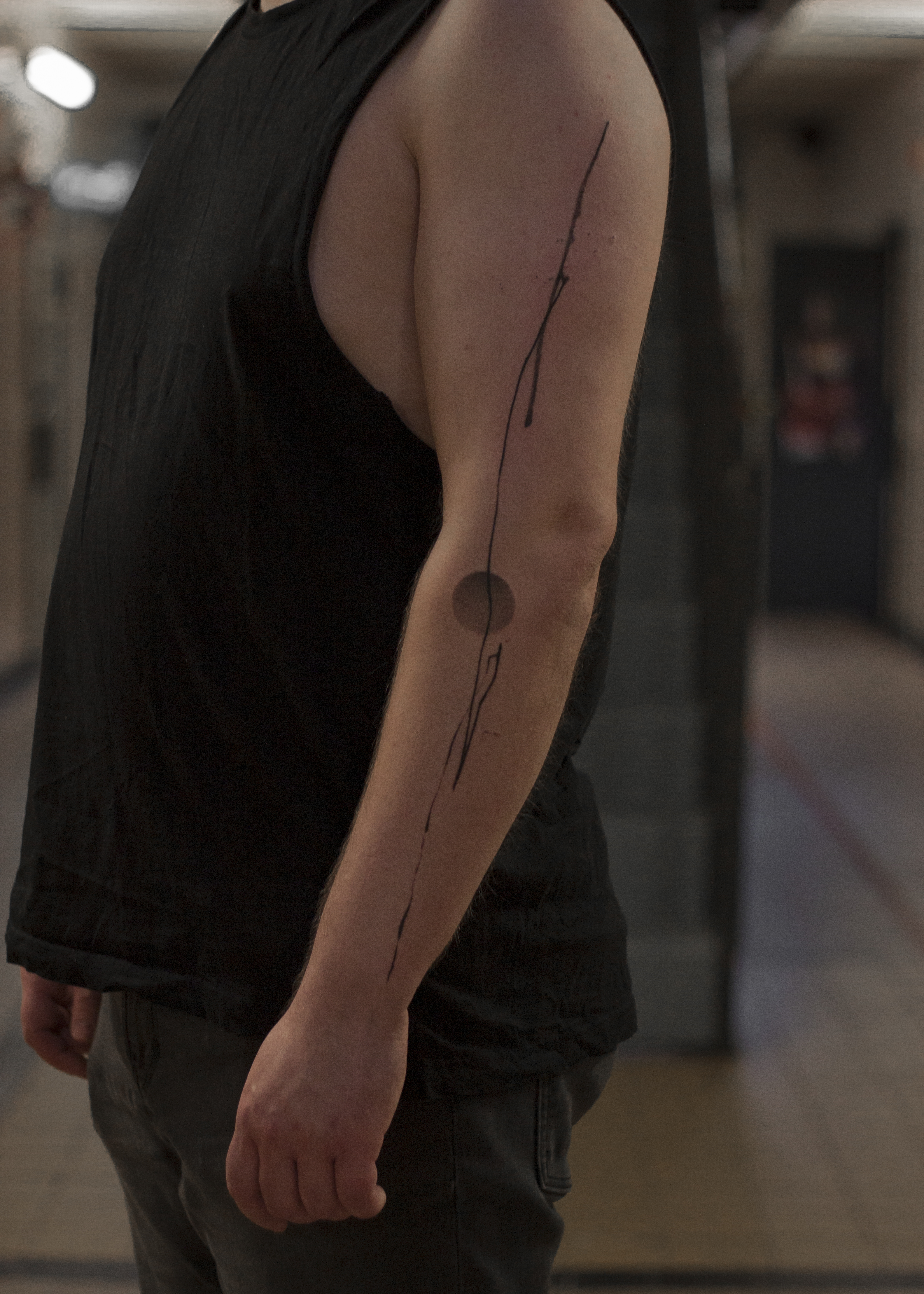 Tattoo op de buitenkant van de linkerarm. Er is een lijn te zien er asl inkt op lijkt geschilderd, er is een cirkel vorm op de achtergrond